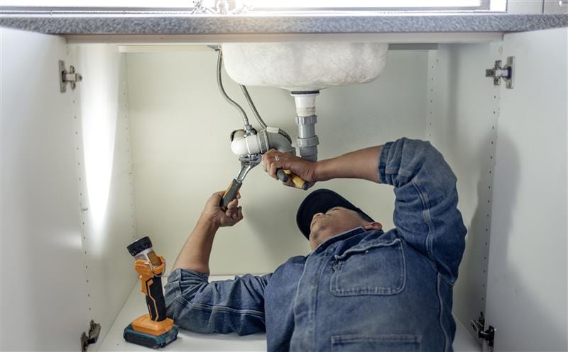 Plumber repairing pipes beneath a bathroom sink in Fontana