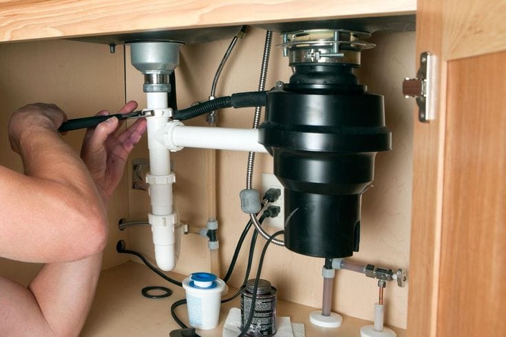 Plumber installing a garbage disposal beneath a kitchen sink in Fontana
