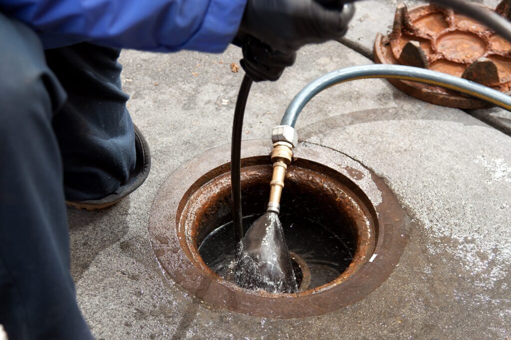 Plumber hydro jetting a sewer line through a manhole in Fontana