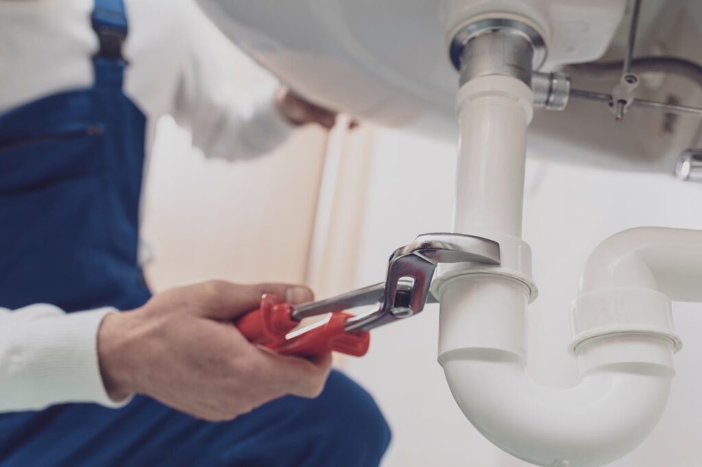Plumber repairing a white drain pipe beneath a sink in Fontana