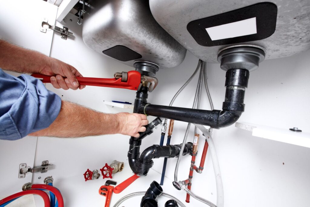 Plumber repairing drain pipes beneath a kitchen sink in Fontana